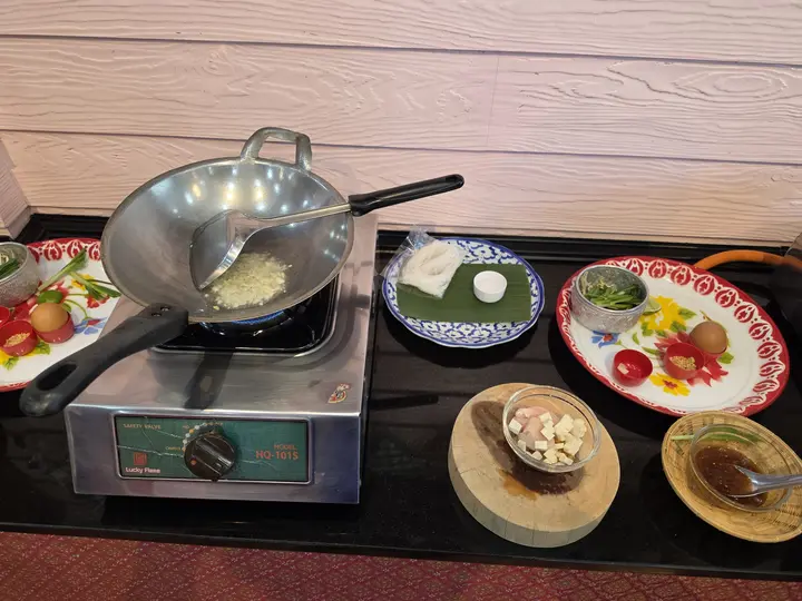 A wok on a gas burner with prepped ingredients at a cooking class station