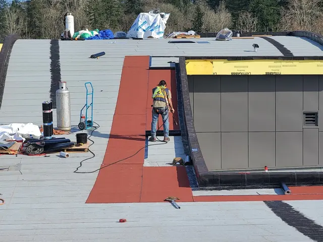 Roof membrane installation beside a rooftop mechanical enclosure.