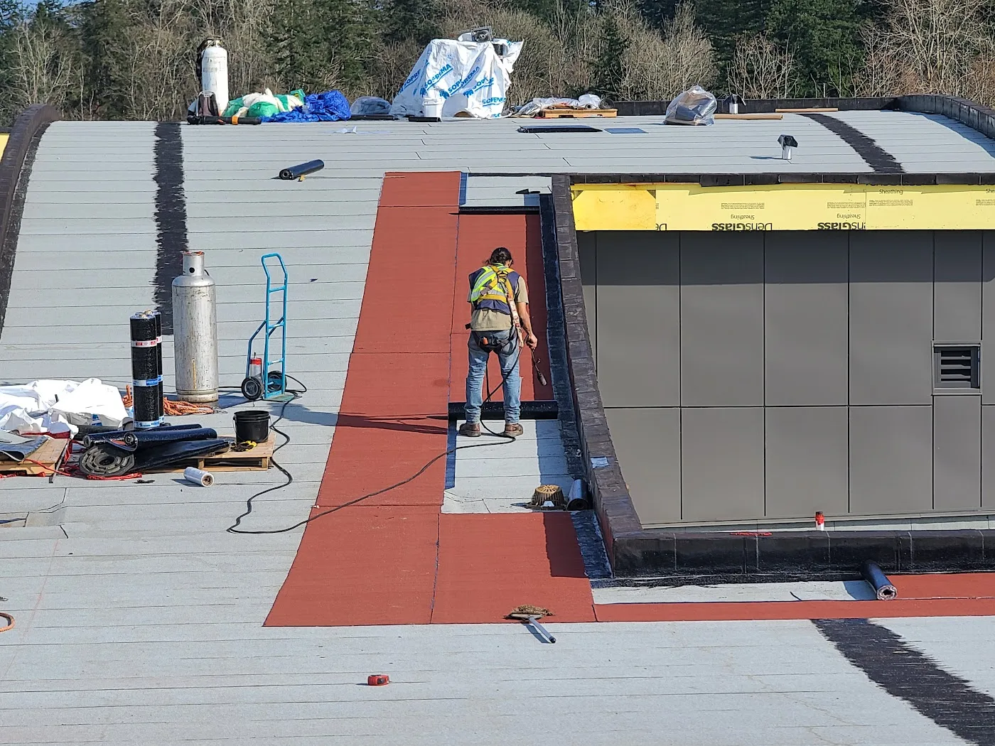 Roof membrane installation beside a rooftop mechanical enclosure.