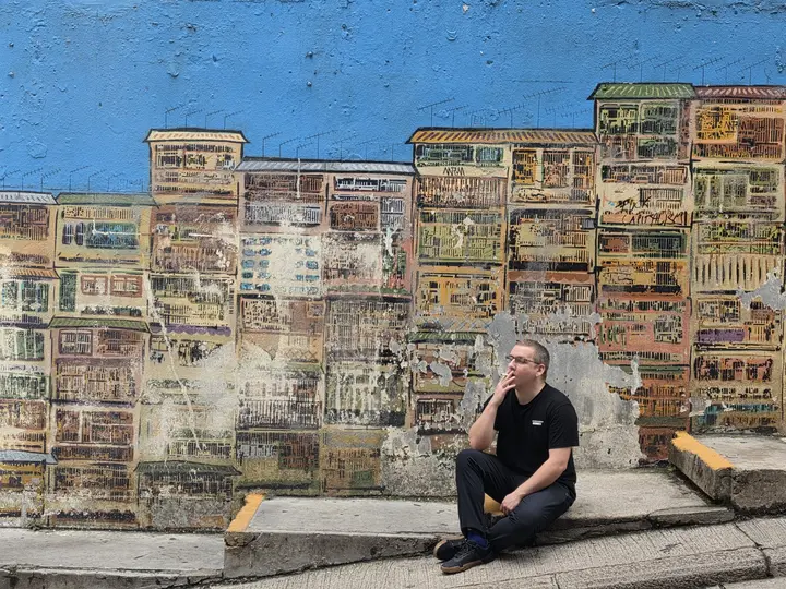 Jeremy sitting on a step in front of a painted wall of old tenement windows