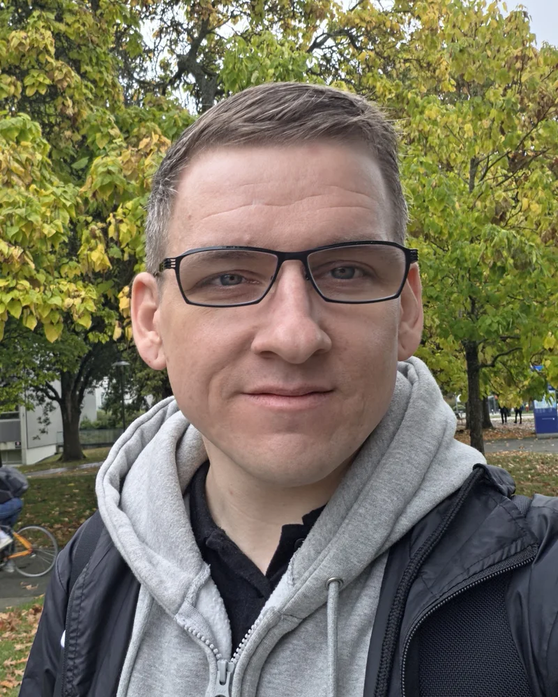 Jeremy in glasses and a grey hoodie, outdoors under autumn trees