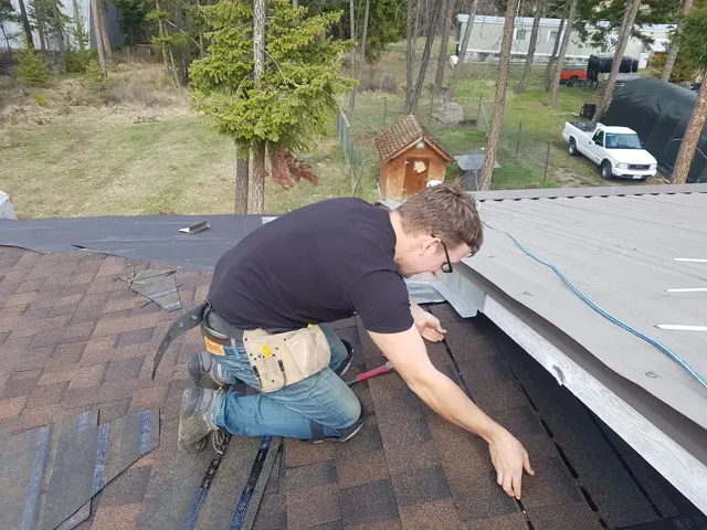 Roof work along the edge of a dark shingle roof.